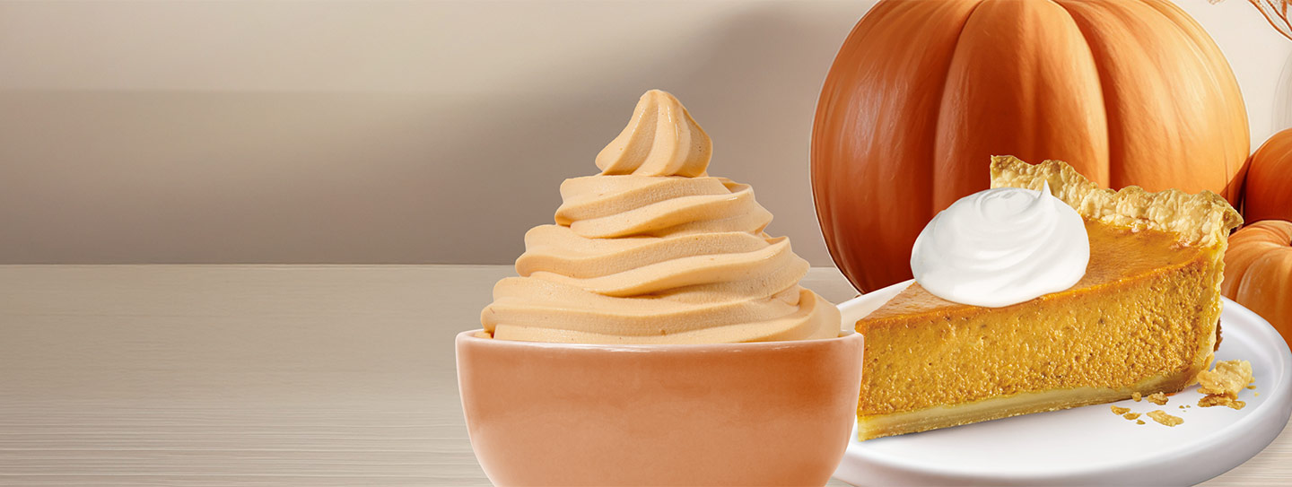 A cup of frozen yogurt alongside a slice of pumpkin pie and pumpkins.