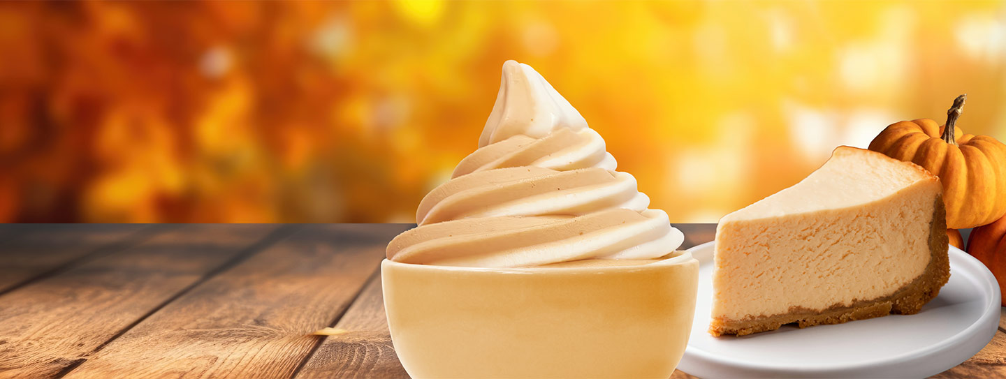 A cup of frozen yogurt alongside a slice of pumpkin pie and pumpkins.
