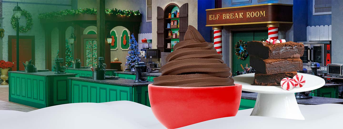 A cup of frozen yogurt alongside a plate of brownies and peppermint candy, in front of a Santa's workshop-themed kitchen